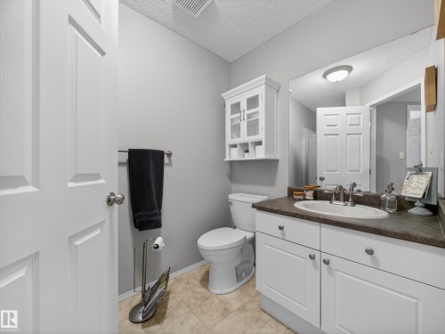 The bathroom features a vanity with white cabinetry and a dark countertop, a toilet, and a wall-mounted storage cabinet - 1665 Tompkins Place, Edmonton, AB - Indoor Photo Showing Bathroom