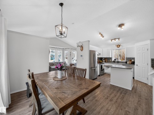 Open concept living area featuring a dining space with a wooden table, a kitchen with white cabinetry and stainless steel appliances, and wood-look flooring throughout - 1665 Tompkins Place, Edmonton, AB - Indoor Photo Showing Dining Room