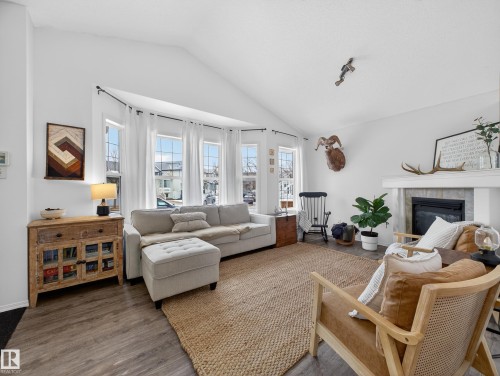 The living area features a vaulted ceiling, wood-style flooring, and a fireplace with a light-colored mantel - 1665 Tompkins Place, Edmonton, AB - Indoor Photo Showing Living Room With Fireplace