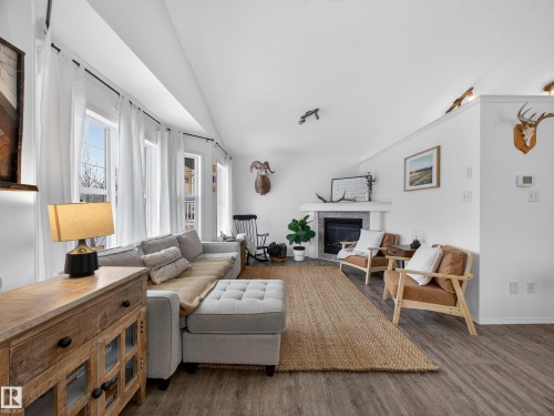 The property features a spacious living area with large windows, a fireplace with a mantel, and durable flooring - 1665 Tompkins Place, Edmonton, AB - Indoor Photo Showing Living Room With Fireplace