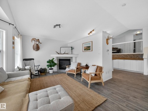 This inviting living area features a fireplace with a tiled surround and white mantle, light-toned walls, and wood-look flooring - 1665 Tompkins Place, Edmonton, AB - Indoor Photo Showing Living Room With Fireplace