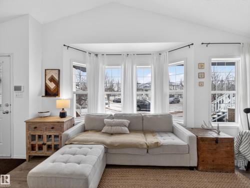 Living area with vaulted ceilings, bay windows providing natural light, and warm tone flooring - 1665 Tompkins Place, Edmonton, AB - Indoor Photo Showing Living Room