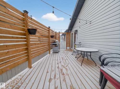 The property features a wooden deck with a privacy fence and string lights, leading to a white gate - 1665 Tompkins Place, Edmonton, AB - Outdoor With Deck Patio Veranda With Exterior