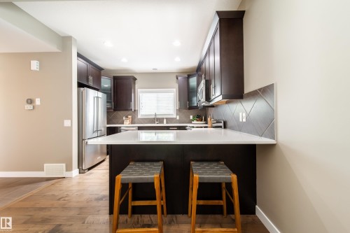 The kitchen features dark wood cabinetry, stainless steel appliances, a white countertop, and a tiled backsplash - 3451 Cutler Crescent, Edmonton, AB - Indoor Photo Showing Kitchen With Upgraded Kitchen