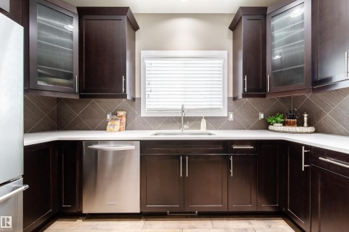 The kitchen features dark wood cabinetry, white countertops, and a tiled backsplash with a diagonal pattern - 3451 Cutler Crescent, Edmonton, AB - Indoor Photo Showing Kitchen With Upgraded Kitchen
