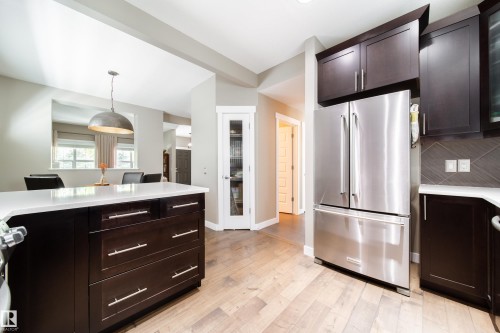 The kitchen features rich dark cabinetry, light hardwood flooring, and a stainless steel refrigerator - 3451 Cutler Crescent, Edmonton, AB - Indoor Photo Showing Kitchen With Stainless Steel Kitchen With Upgraded Kitchen
