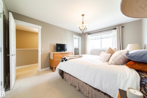 The property features a bedroom with light-colored carpeting, a window with curtains, and a chandelier light fixture - 3451 Cutler Crescent, Edmonton, AB - Indoor Photo Showing Bedroom