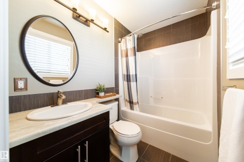 The bathroom features a vanity with a dark wood cabinet and a light-colored countertop, a white oval sink, and a round mirror - 3451 Cutler Crescent, Edmonton, AB - Indoor Photo Showing Bathroom
