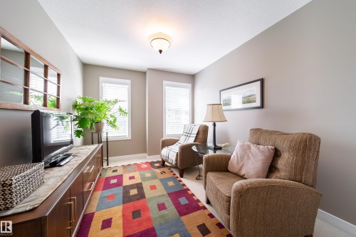 This inviting room features neutral-toned walls, two windows with blinds, and a colorful geometric area rug - 3451 Cutler Crescent, Edmonton, AB - Indoor