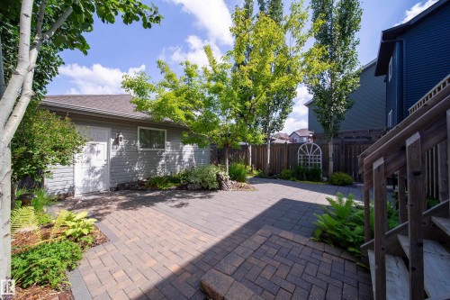 The property includes a paved patio area, a detached garage with siding and a shingled roof, and landscaping with various plants and mature trees - 3451 Cutler Crescent, Edmonton, AB - Outdoor