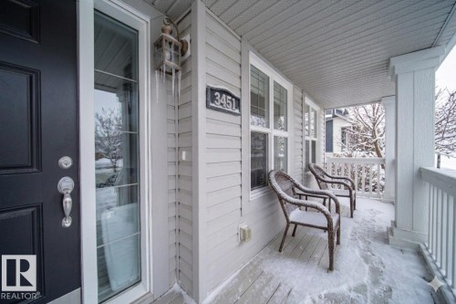 The property features a welcoming front porch with white railings and two chairs, alongside a dark-colored entry door with a decorative glass insert - 3451 Cutler Crescent, Edmonton, AB - Outdoor With Exterior