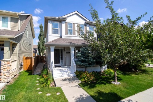 The property features a well-maintained lawn and mature trees, a paved pathway leading to the front entrance, and a covered porch with white railings - 3451 Cutler Crescent, Edmonton, AB - Outdoor