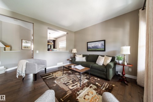This living area features rich hardwood floors, a neutral wall color, and an open pass-through to an additional room - 3451 Cutler Crescent, Edmonton, AB - Indoor Photo Showing Living Room
