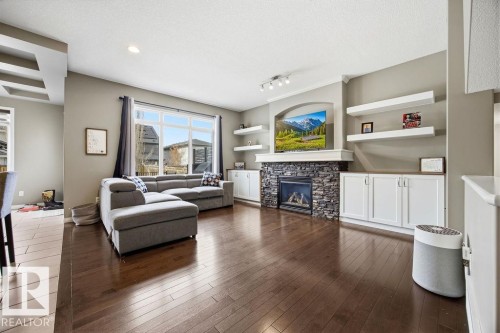 Living room featuring rich hardwood floors, a stone-faced fireplace, and built-in shelving and cabinetry - 13024 206 Street, Edmonton, AB - Indoor Photo Showing Living Room With Fireplace
