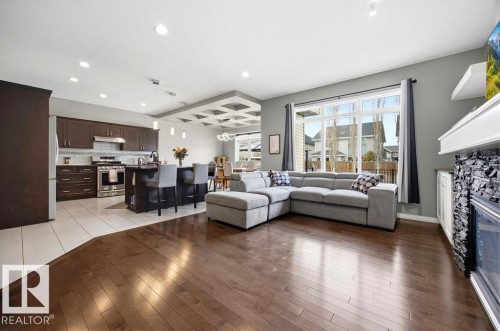 Spacious open concept living area featuring hardwood flooring, large windows, and a kitchen with stainless steel appliances, dark cabinetry, and an island with seating - 13024 206 Street, Edmonton, AB - Indoor Photo Showing Living Room