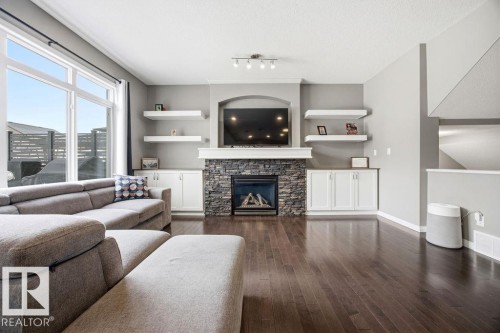 Living area featuring hardwood floors, a stone fireplace, built-in cabinetry, and large windows providing natural light - 13024 206 Street, Edmonton, AB - Indoor Photo Showing Living Room With Fireplace