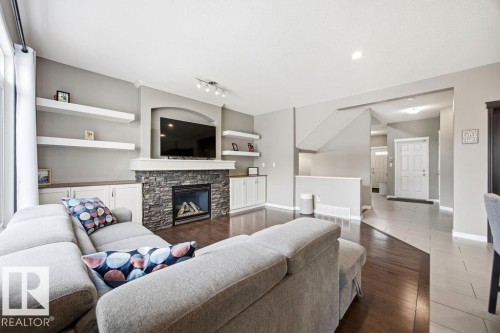 Living room featuring dark hardwood floors, a stone-faced fireplace with a mantel, and built-in white cabinetry with open shelving - 13024 206 Street, Edmonton, AB - Indoor Photo Showing Living Room With Fireplace