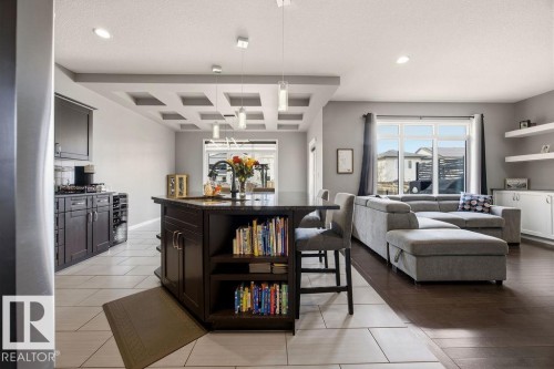 This inviting open-concept space features dark wood cabinetry, a kitchen island with seating, a decorative ceiling, and large windows that provide abundant natural light - 13024 206 Street, Edmonton, AB - Indoor Photo Showing Living Room
