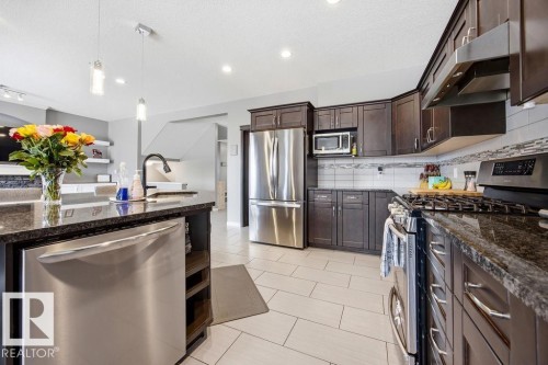 The kitchen features dark wood cabinetry, stainless steel appliances, and granite countertops - 13024 206 Street, Edmonton, AB - Indoor Photo Showing Kitchen With Stainless Steel Kitchen With Upgraded Kitchen