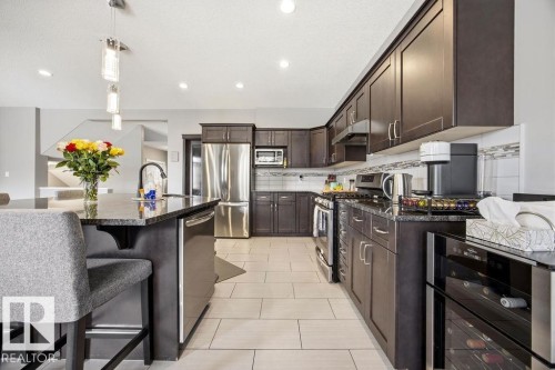 Spacious kitchen featuring dark wood cabinetry, granite countertops, stainless steel appliances, and light-colored tile flooring - 13024 206 Street, Edmonton, AB - Indoor Photo Showing Kitchen With Stainless Steel Kitchen With Upgraded Kitchen