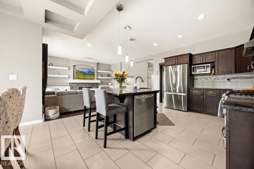 The kitchen features dark wood cabinetry, stainless steel appliances, and a central island with bar seating - 13024 206 Street, Edmonton, AB - Indoor Photo Showing Kitchen With Stainless Steel Kitchen With Upgraded Kitchen