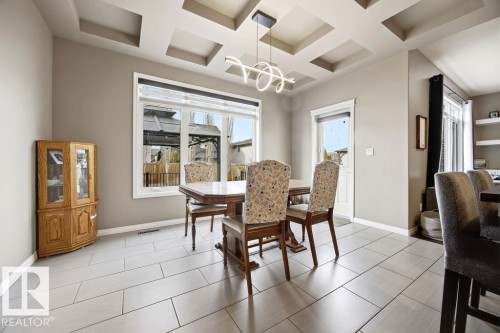The dining area features light-colored rectangular tile flooring, a coffered ceiling with a modern light fixture, and a large window providing ample natural light - 13024 206 Street, Edmonton, AB - Indoor Photo Showing Dining Room