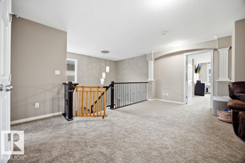 Open concept living area featuring neutral carpeting, a staircase with dark wood and metal railing, and an arched doorway with decorative pillars - 13024 206 Street, Edmonton, AB - Indoor Photo Showing Other Room