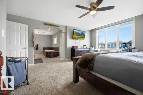 This inviting space features light-colored carpet, a ceiling fan with integrated lighting, and a large window providing views of the neighborhood - 13024 206 Street, Edmonton, AB - Indoor Photo Showing Bedroom