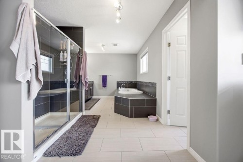 Spacious bathroom featuring a glass-enclosed shower, a corner built-in tub, and light-colored tiled flooring - 13024 206 Street, Edmonton, AB - Indoor