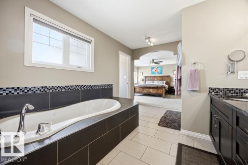 Bathroom featuring a built-in tub with tile surround and mosaic accent, a window providing natural light, and a vanity with a dark countertop - 13024 206 Street, Edmonton, AB - Indoor Photo Showing Bathroom