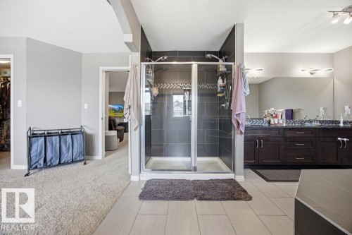 Expansive bathroom featuring a spacious walk-in shower with dark tile surround, a large vanity with double sinks and extensive counter space, and light-colored floor tiling - 13024 206 Street, Edmonton, AB - Indoor Photo Showing Bathroom