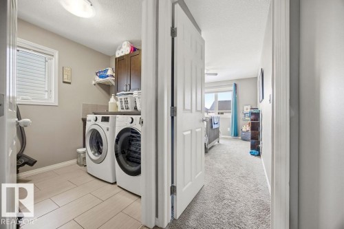 Practical laundry area with tiled flooring, a window providing natural light, and dark wood cabinetry for storage - 13024 206 Street, Edmonton, AB - Indoor Photo Showing Laundry Room