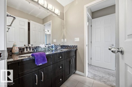 The bathroom features a dark wood vanity with a granite countertop, dual sinks, and a tiled backsplash - 13024 206 Street, Edmonton, AB - Indoor Photo Showing Bathroom