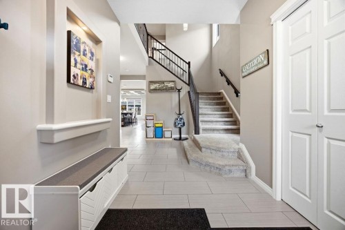 Inviting entryway featuring light-toned walls, tile flooring, and a carpeted staircase with a dark banister - 13024 206 Street, Edmonton, AB - Indoor Photo Showing Other Room
