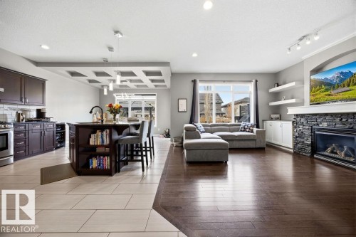 Open concept living space featuring a kitchen with a dark wood island and cabinetry, and a living area with dark wood flooring and a stone fireplace - 13024 206 Street, Edmonton, AB - Indoor Photo Showing Living Room With Fireplace