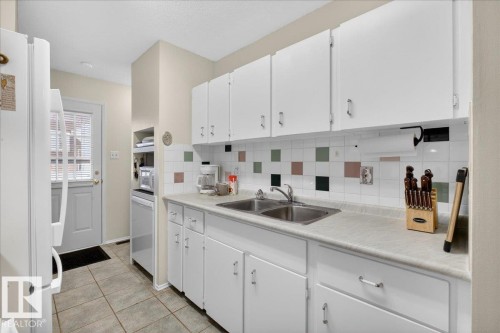 The kitchen features white cabinetry, a double basin sink, and a tiled backsplash with decorative square accents - 2 Mcleod Place, Edmonton, AB - Indoor Photo Showing Kitchen With Double Sink