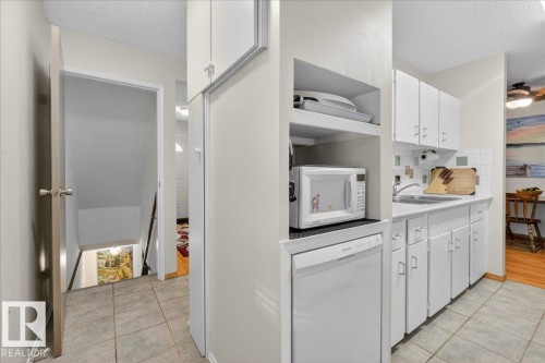 The kitchen features white cabinetry, a sink, and a tiled backsplash, with a dishwasher integrated below the counter - 2 Mcleod Place, Edmonton, AB - Indoor Photo Showing Kitchen