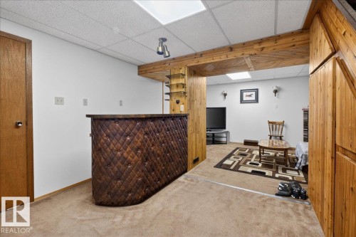 This versatile space features a built-in bar with a diamond-tufted facade, carpeted flooring, and wood paneling - 2 Mcleod Place, Edmonton, AB - Indoor Photo Showing Other Room