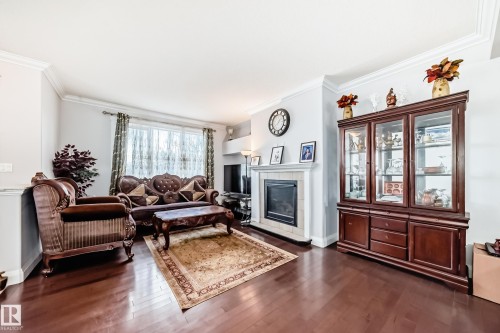 The living area features polished hardwood floors, a fireplace with a light-colored tile surround, and a large window providing natural light - 2 12042 101 Street, Edmonton, AB - Indoor Photo Showing Living Room With Fireplace