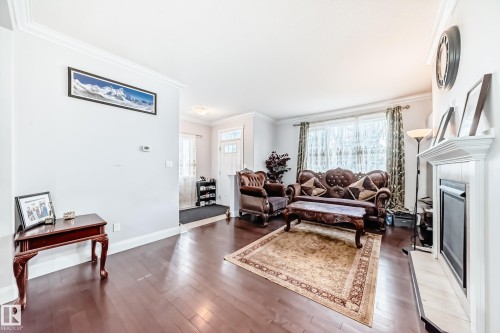 Living room featuring hardwood floors, a fireplace with a white mantel, and a window with patterned curtains - 2 12042 101 Street, Edmonton, AB - Indoor Photo Showing Living Room With Fireplace