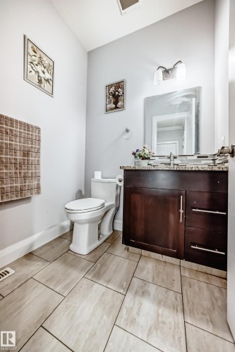 Bathroom featuring tile flooring, a dark wood vanity with a granite countertop, a toilet, and a vanity mirror - 2 12042 101 Street, Edmonton, AB - Indoor Photo Showing Bathroom