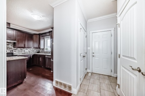 The property features a kitchen with dark wood cabinetry, light-colored countertops, and a mosaic tile backsplash, visible from an entryway with light-colored tile flooring - 2 12042 101 Street, Edmonton, AB - Indoor Photo Showing Other Room