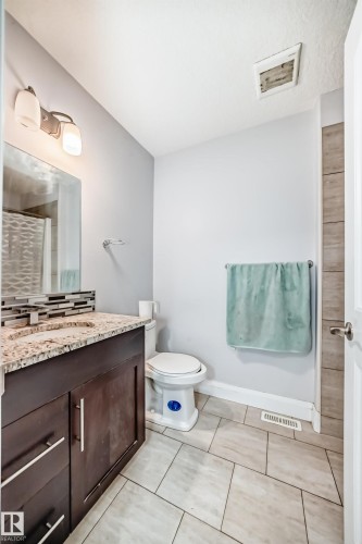 Bathroom featuring a dark wood vanity with a granite countertop, a rectangular sink, and a tiled backsplash - 2 12042 101 Street, Edmonton, AB - Indoor Photo Showing Bathroom