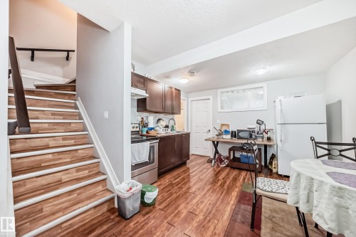 This kitchen features wood-look flooring, dark wood cabinetry, and a white refrigerator - 2 12042 101 Street, Edmonton, AB - Indoor