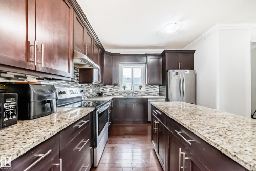 The kitchen features rich wood cabinetry, granite countertops, and a mosaic tile backsplash - 2 12042 101 Street, Edmonton, AB - Indoor Photo Showing Kitchen With Stainless Steel Kitchen With Upgraded Kitchen