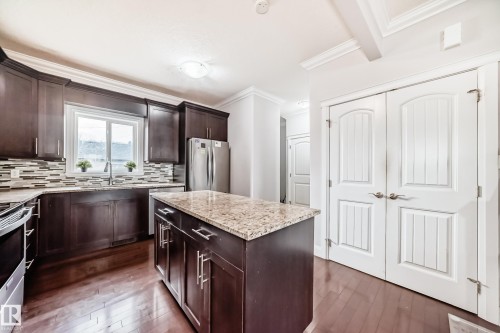 The kitchen features dark wood cabinetry, a central island with a light-colored countertop, and a stainless steel refrigerator - 2 12042 101 Street, Edmonton, AB - Indoor Photo Showing Kitchen With Double Sink With Upgraded Kitchen