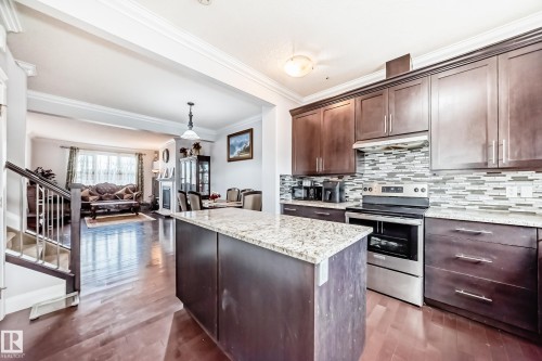 This property features hardwood flooring, a kitchen with dark cabinetry, granite countertops, a tiled backsplash, and stainless steel appliances - 2 12042 101 Street, Edmonton, AB - Indoor Photo Showing Kitchen With Upgraded Kitchen