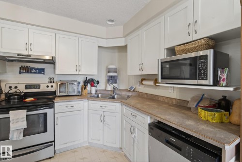 The kitchen features white cabinetry, a double basin stainless steel sink, and a stainless steel oven with an overhead range hood - 2006 Mill Woods Road E, Edmonton, AB - Indoor Photo Showing Kitchen With Double Sink