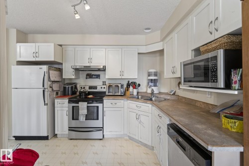 The kitchen features white cabinetry, a double basin sink, and a range with a stainless steel finish - 2006 Mill Woods Road E, Edmonton, AB - Indoor Photo Showing Kitchen With Double Sink