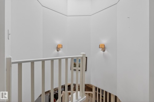 The property features a staircase with white railings, illuminated by two wall-mounted light fixtures - 2006 Mill Woods Road E, Edmonton, AB - Indoor Photo Showing Other Room